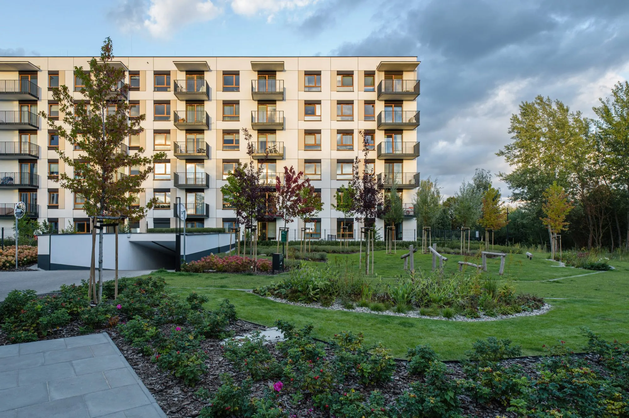 Harmonia Mokotów residential development in Warsaw, completed for Dom Development: a building with balconies facing a green courtyard and the entrance to the underground car park, next to an elevation drawing from the design
